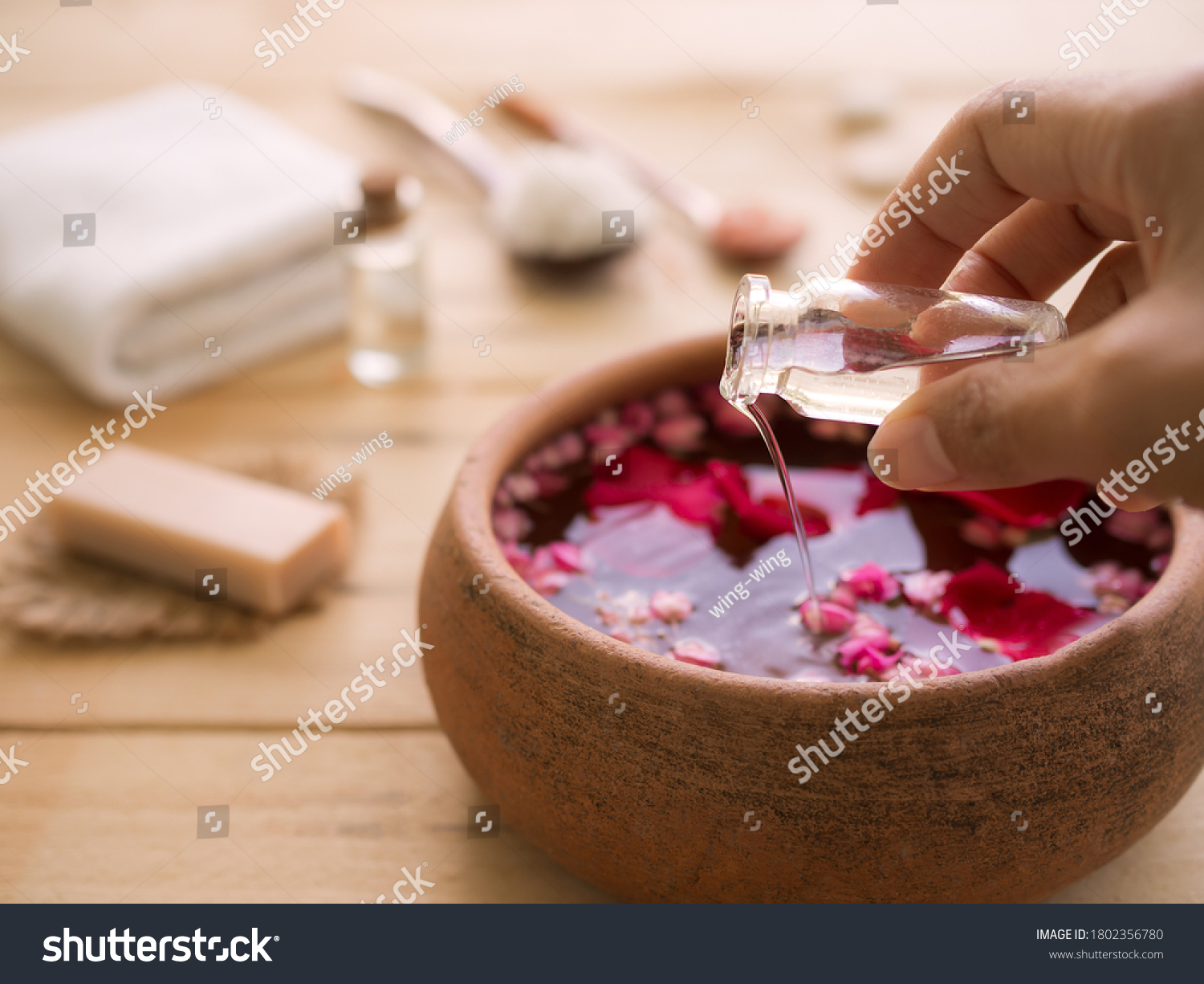 Hand pour coconut oil in to aroma smell rose with blur image of soap, towel, massage oil, salt spa on wood background.  Aroma therapy spa set for luxury hotel or professional massage salons concept. #1802356780