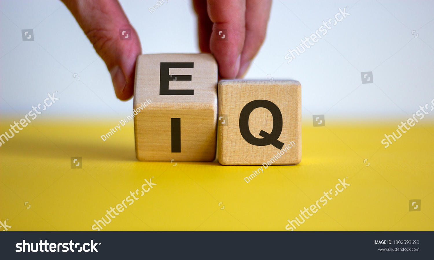 Hand flips a cube and changes the expression 'IQ' to 'EQ'. Beautiful yellow table, white background. Concept of emotional and  intelligence quotient. Copy space. #1802593693
