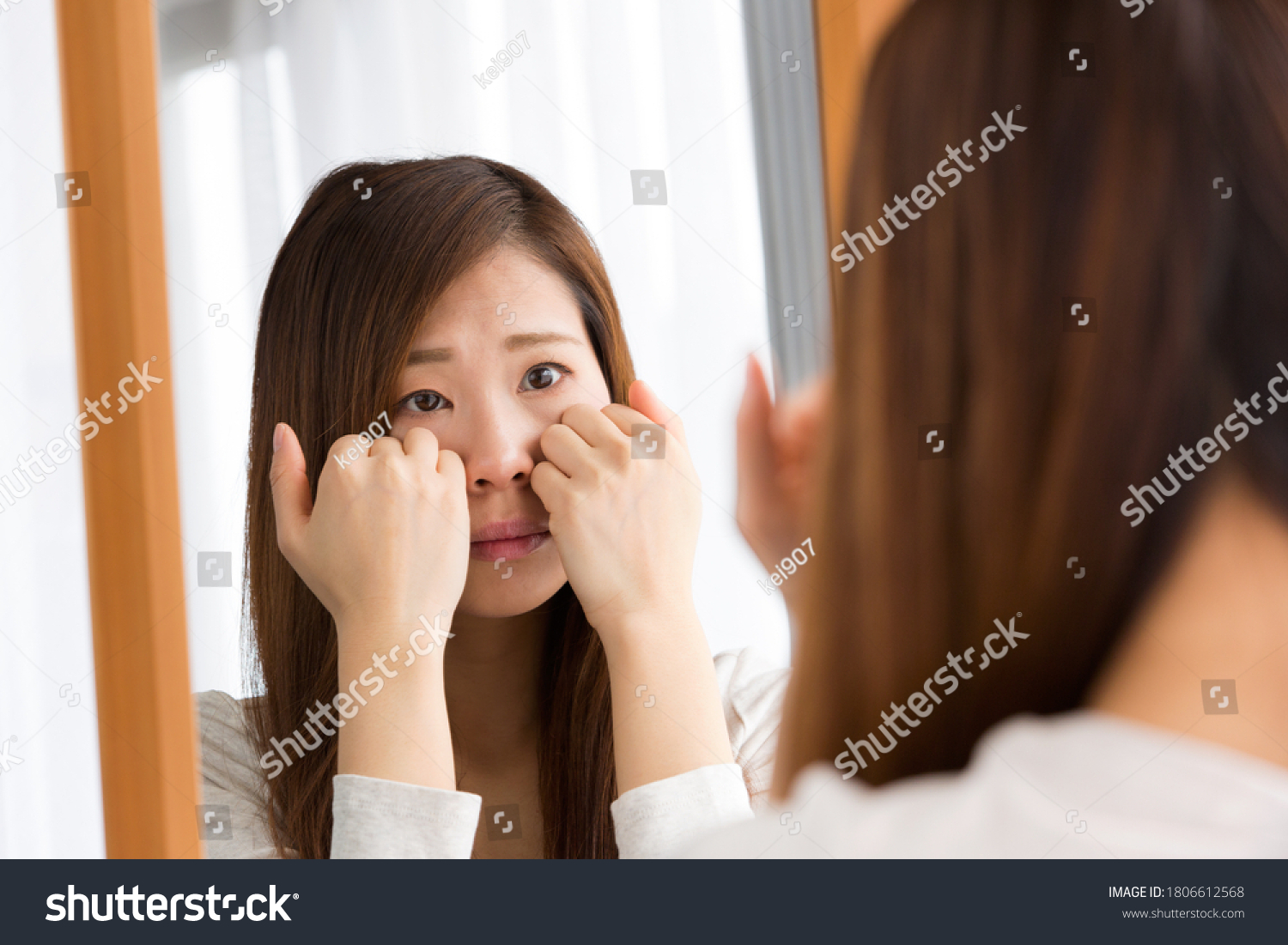 A woman looks at her skin condition in a mirror. #1806612568