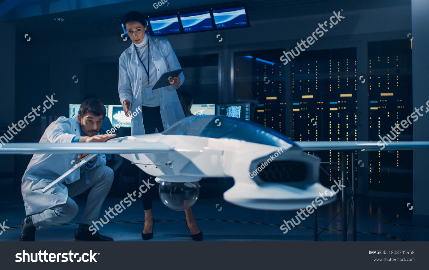 Meeting of Aerospace Engineers Working On Unmanned Aerial Vehicle / Drone Prototype. Aviation Scientists in White Coats Talking. Commercial Aerial Surveillance Aircraft in Industrial Laboratory #1808745958