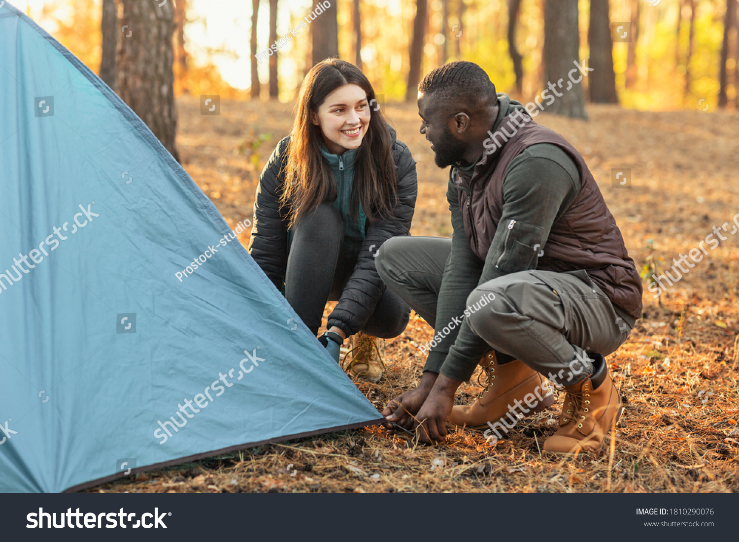 Happy young mixed race couple making tent together, having conversation, camping in forest on weekend #1810290076