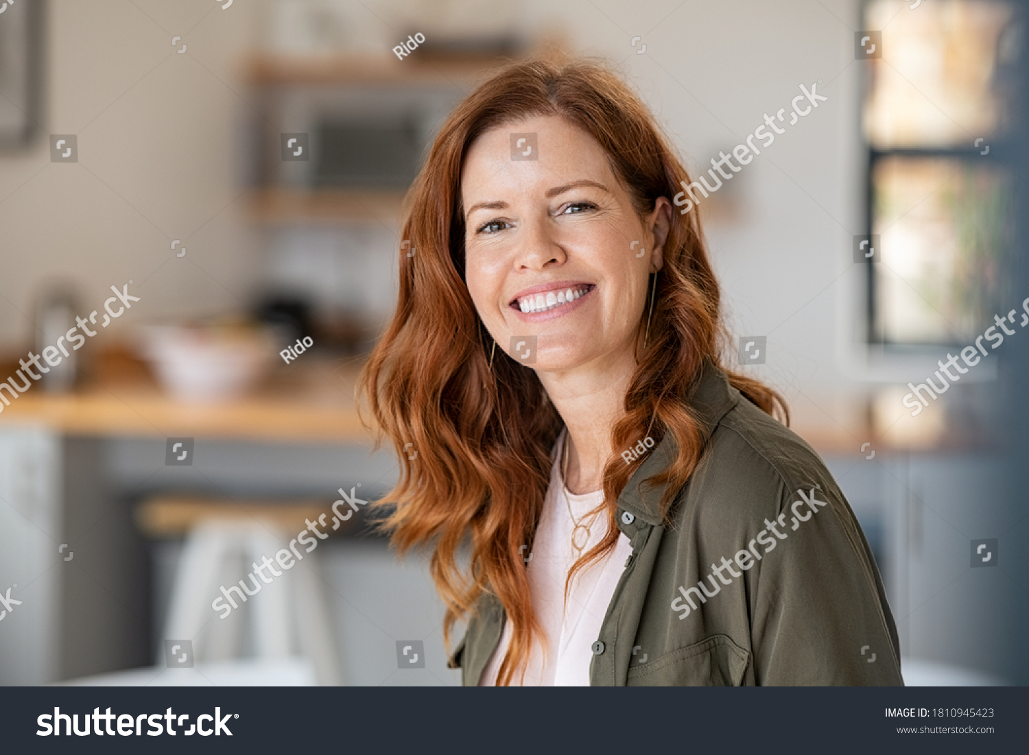 Portrait of smiling mature woman looking at camera with big grin. Successful middle aged woman at home smiling. Beautiful mid adult lady with long red hair enjoying whitening teeth treatment. #1810945423