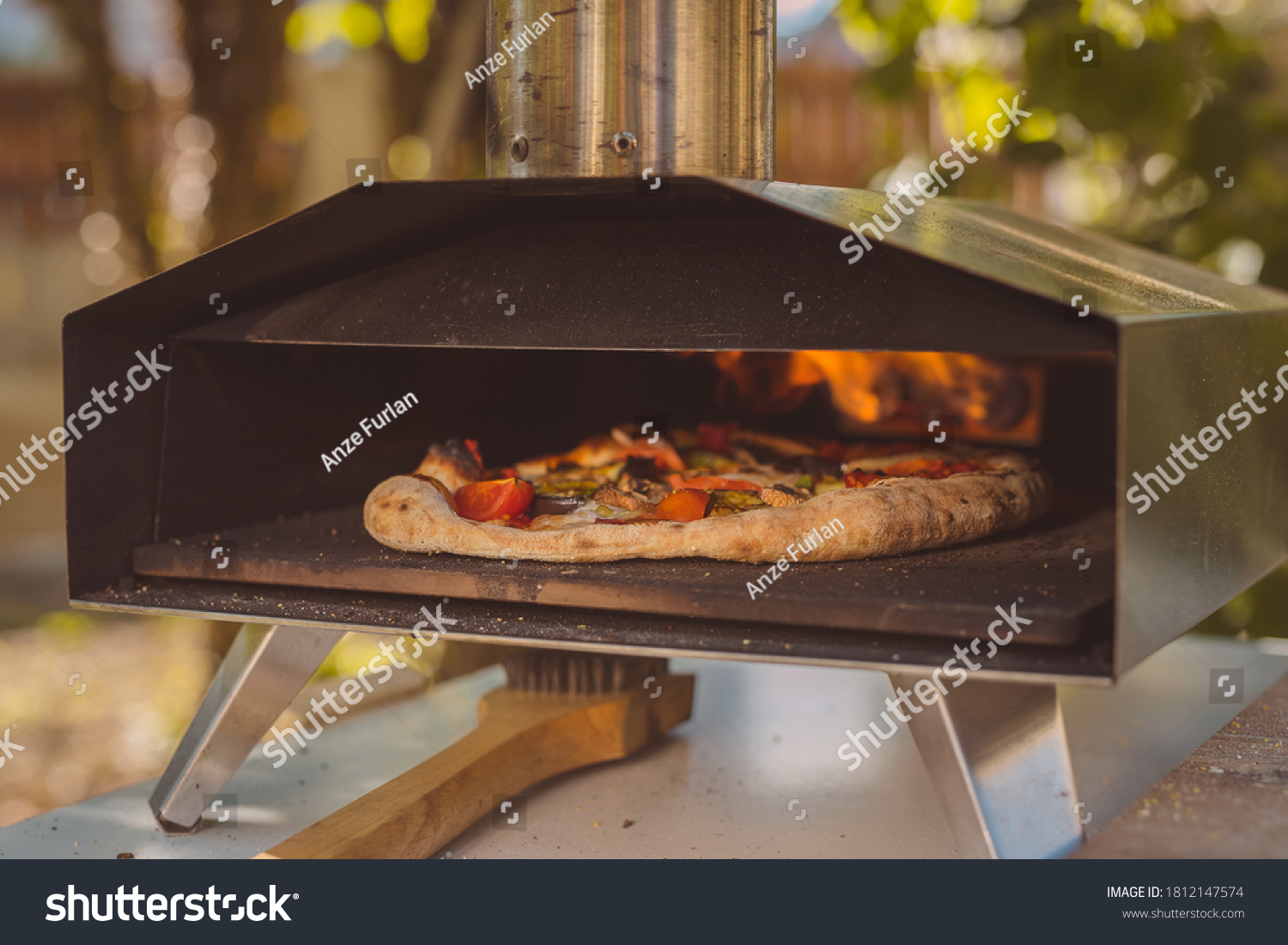 Home made pizza is inserted in a portable aluminium home oven for pizzas. Delicious pizza is baking in an oven, visible fire in the back of the furnace. #1812147574