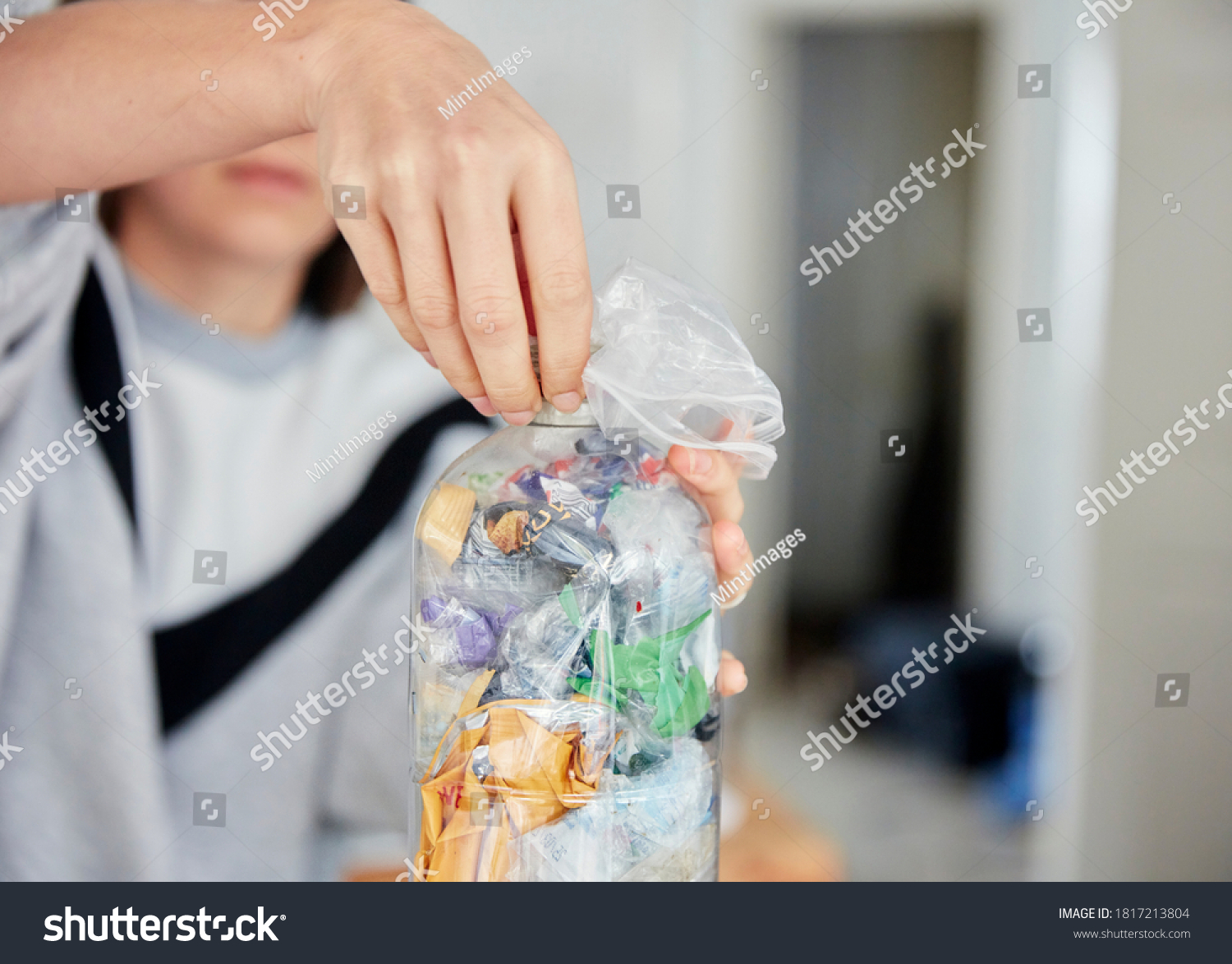 Woman stuffing soft waste plastics into a plastic bottle to make an ecobrick #1817213804