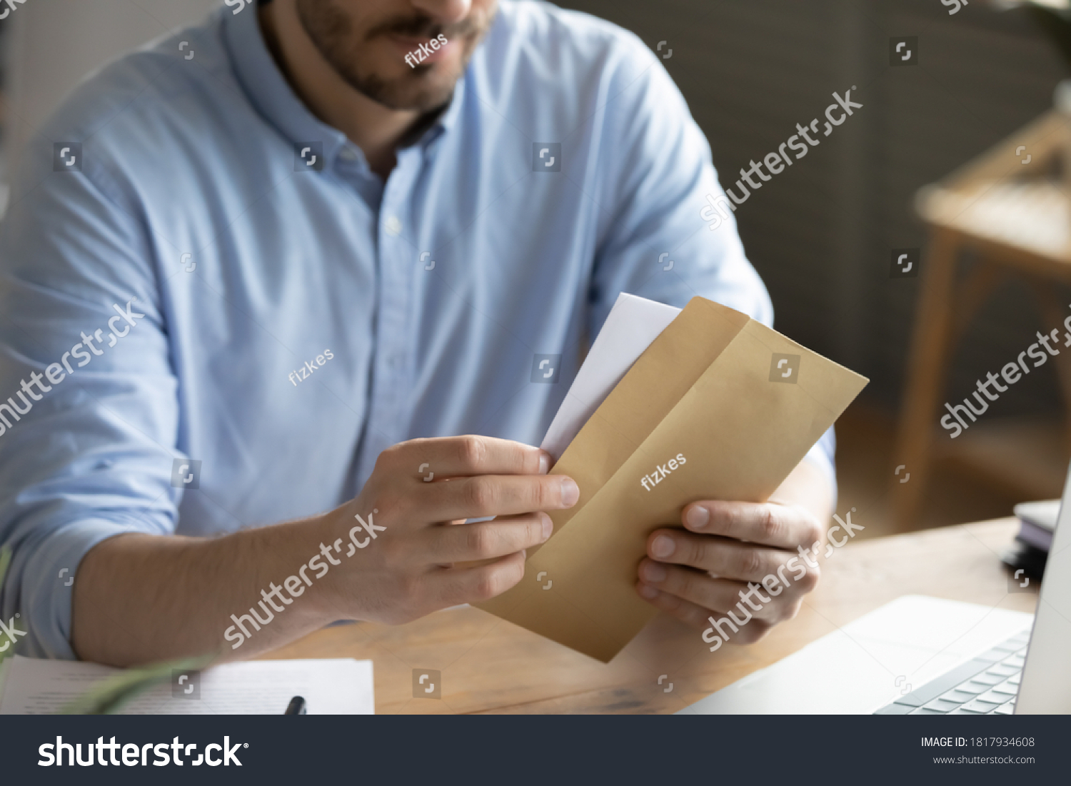 Crop close up of man sit at desk open envelope with paper letter or correspondence at office. Male worker get postal paperwork or notice notification at workplace, receive message or invitation. #1817934608