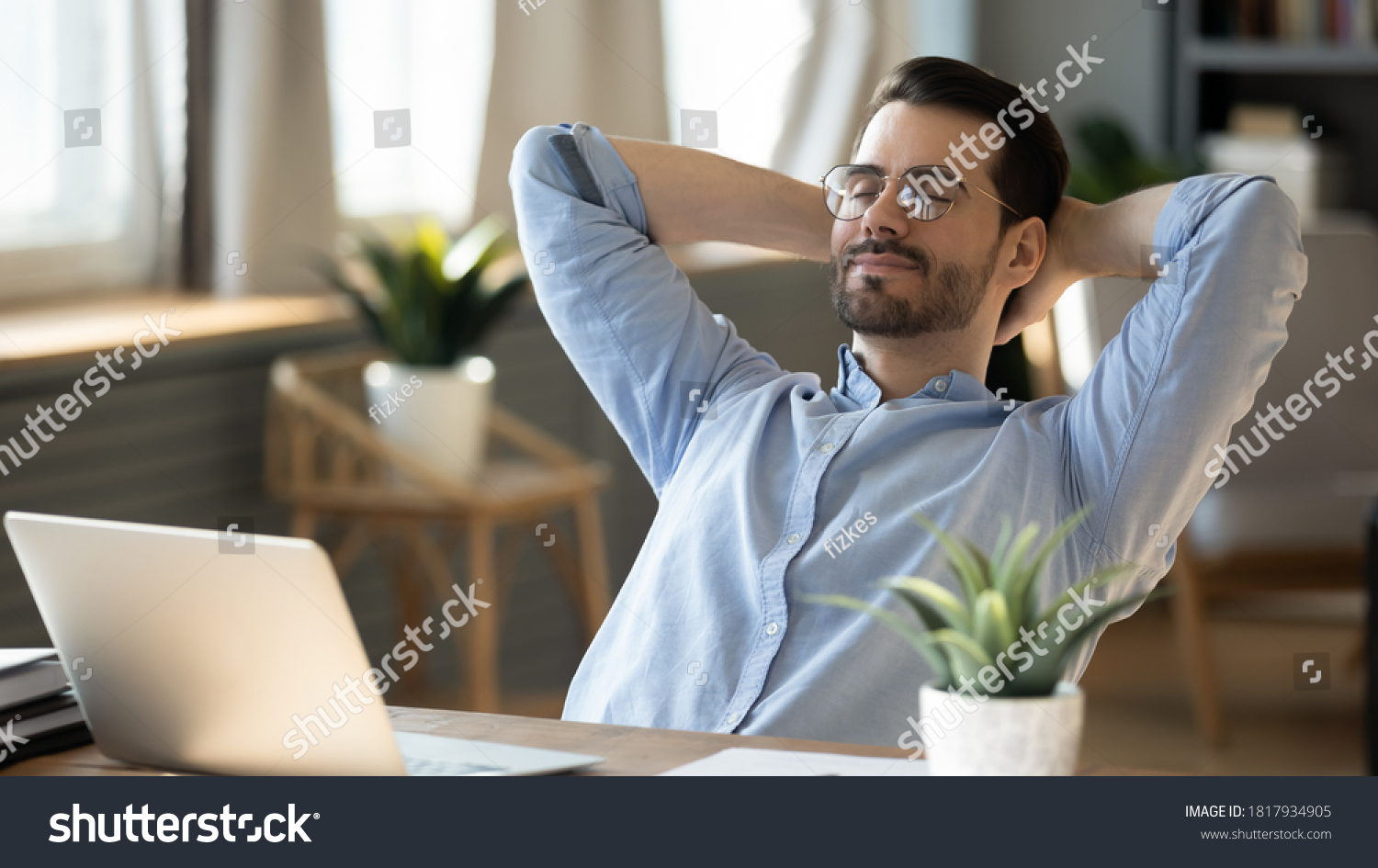 Calm millennial man in glasses sit relax at home office workplace take nap or daydream. Happy relaxed Caucasian young male rest in chair distracted from computer work, relieve negative emotions. #1817934905