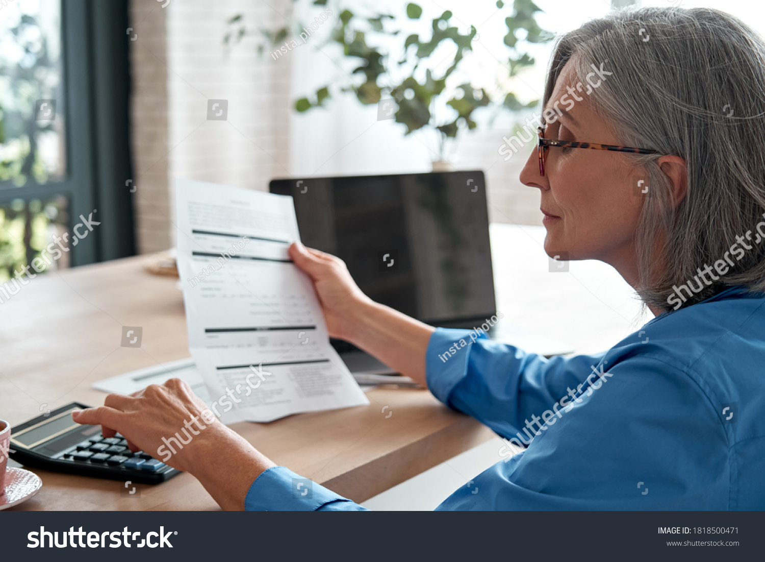Senior mature business woman holding paper bill using calculator, old lady managing account finances, calculating money budget tax, planning banking loan debt pension payment sit at home office table. #1818500471