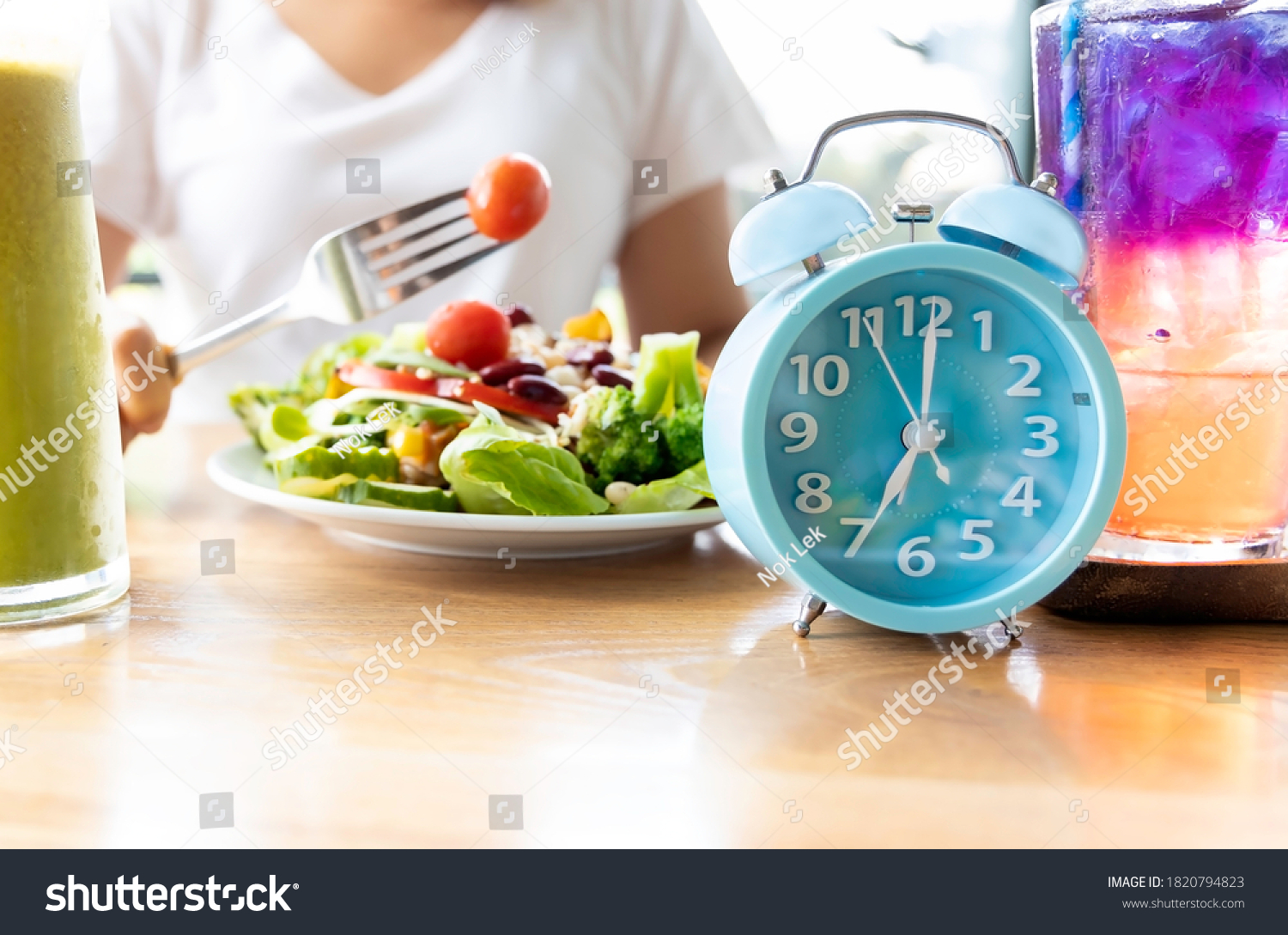 Selective focus of blue clock which woman make a Intermittent fasting with  a Healthy food of salad .Healthy lifestyle Concept. #1820794823