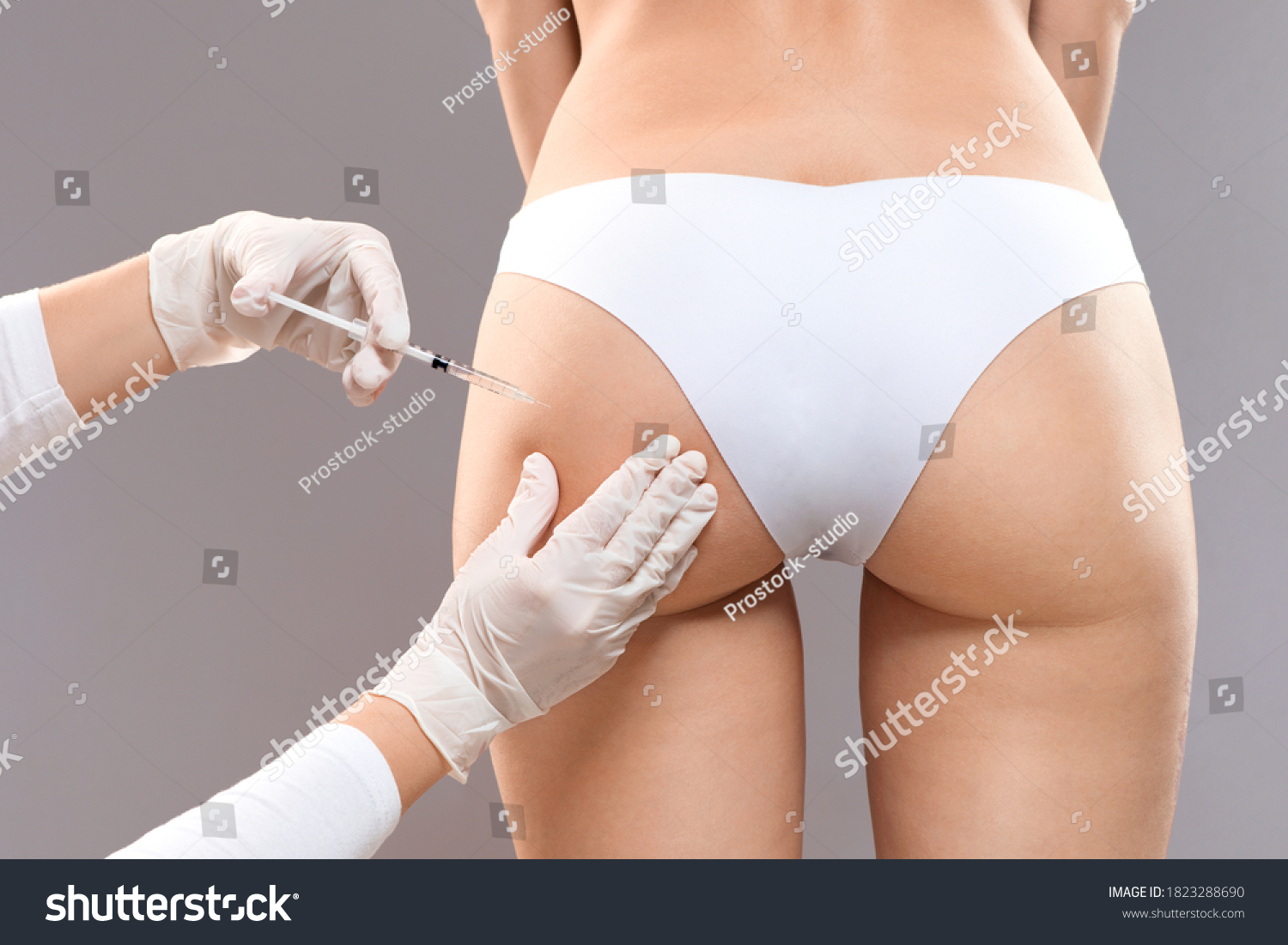 Sculptra butt lifting concept. Slim woman having hip injection at beauty salon, closeup. Plastic surgeon making injection at butt area for unrecognizable lady, grey studio background, back view #1823288690