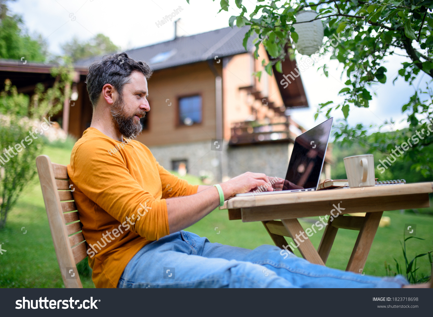 Side view of man with laptop working outdoors in garden, home office concept. #1823718698