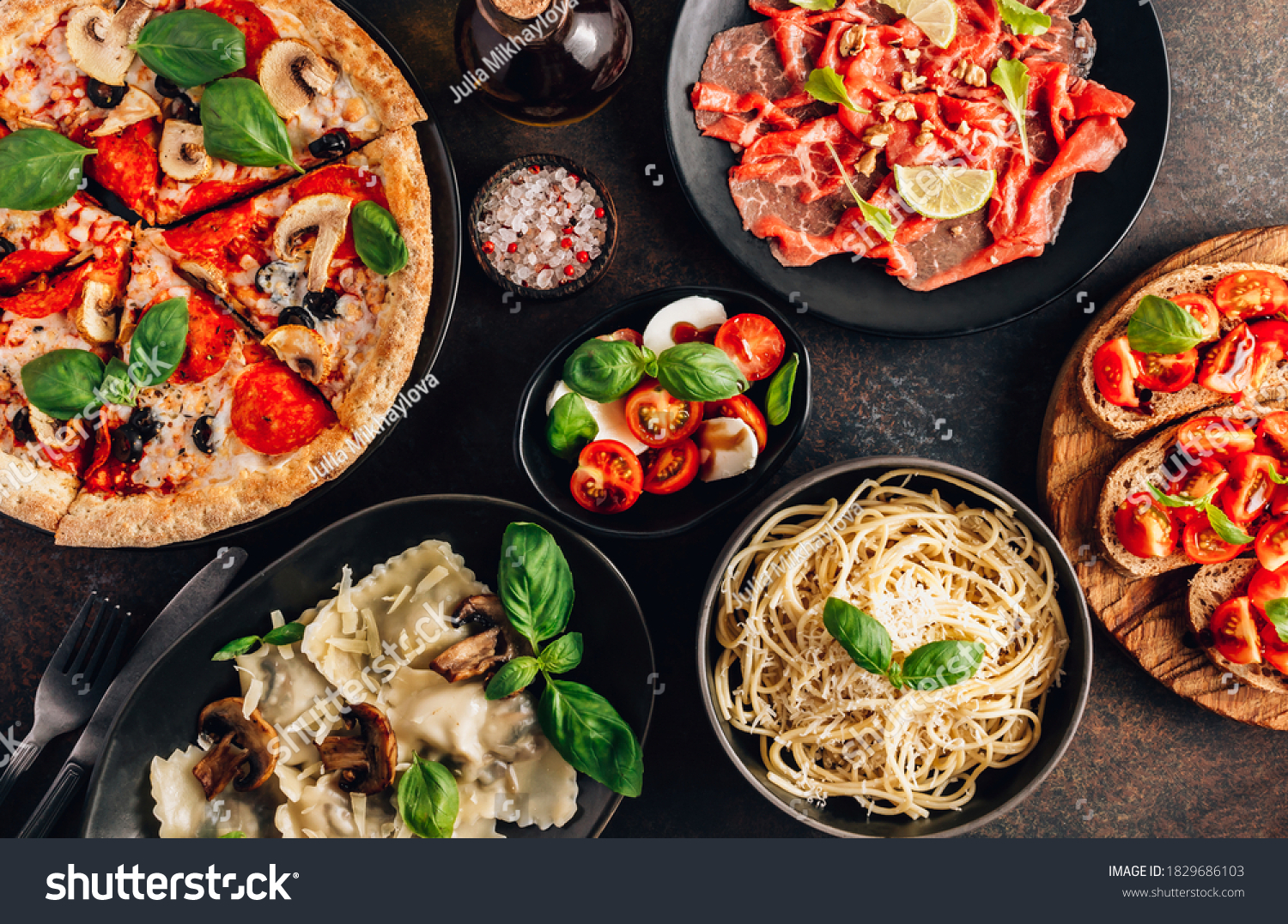 Full table of italian meals on plates Pizza, pasta, ravioli, carpaccio. caprese salad and tomato bruschetta on black background. Top view #1829686103