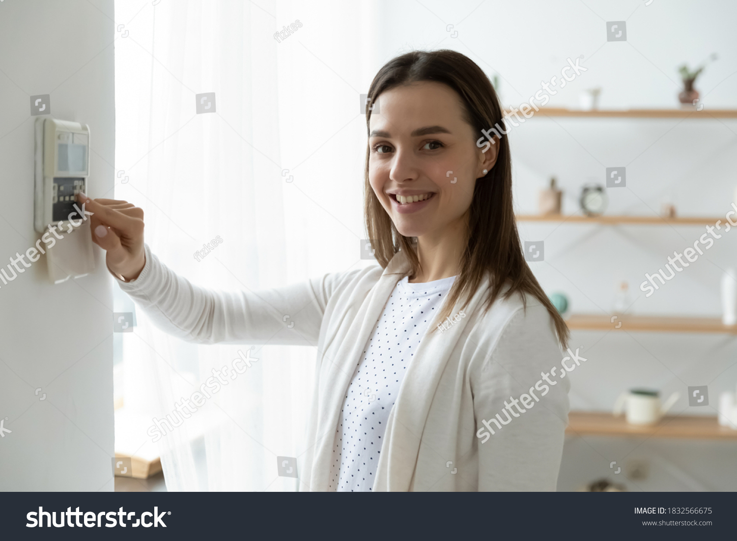 Portrait of smiling young Caucasian woman switch turn on smart home wall control panel. Happy millennial female client use indoors house security system, regulate temperature or activate modern AC. #1832566675