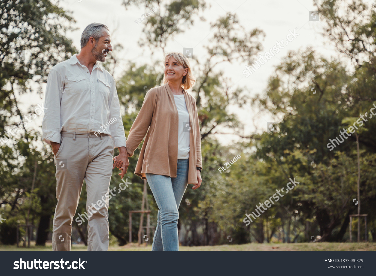 Romantic and elderly healthy lifestyle concept.Senior active caucasian couple holding hands looks happy in the park in the afternoon autumn sunlight,happy anniversary,happily retired with copy space. #1833480829