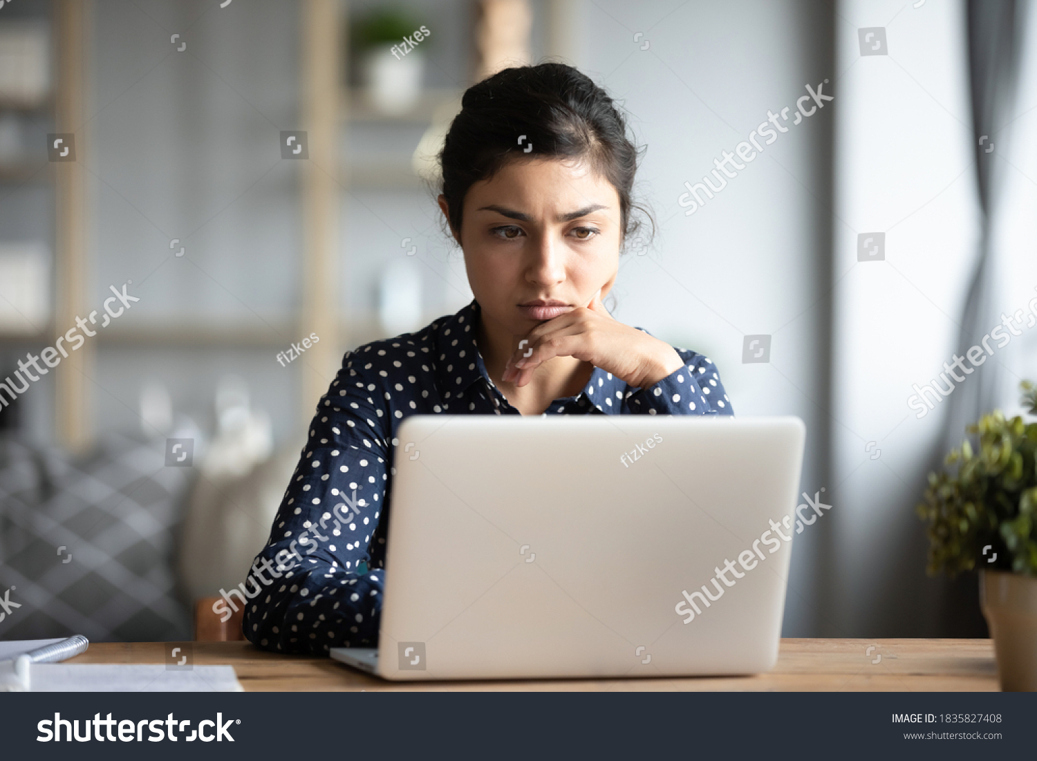Serious frowning indian ethnicity woman sit at workplace desk looks at laptop screen read e-mail feels concerned. Bored unmotivated tired employee, problems difficulties with app understanding concept #1835827408