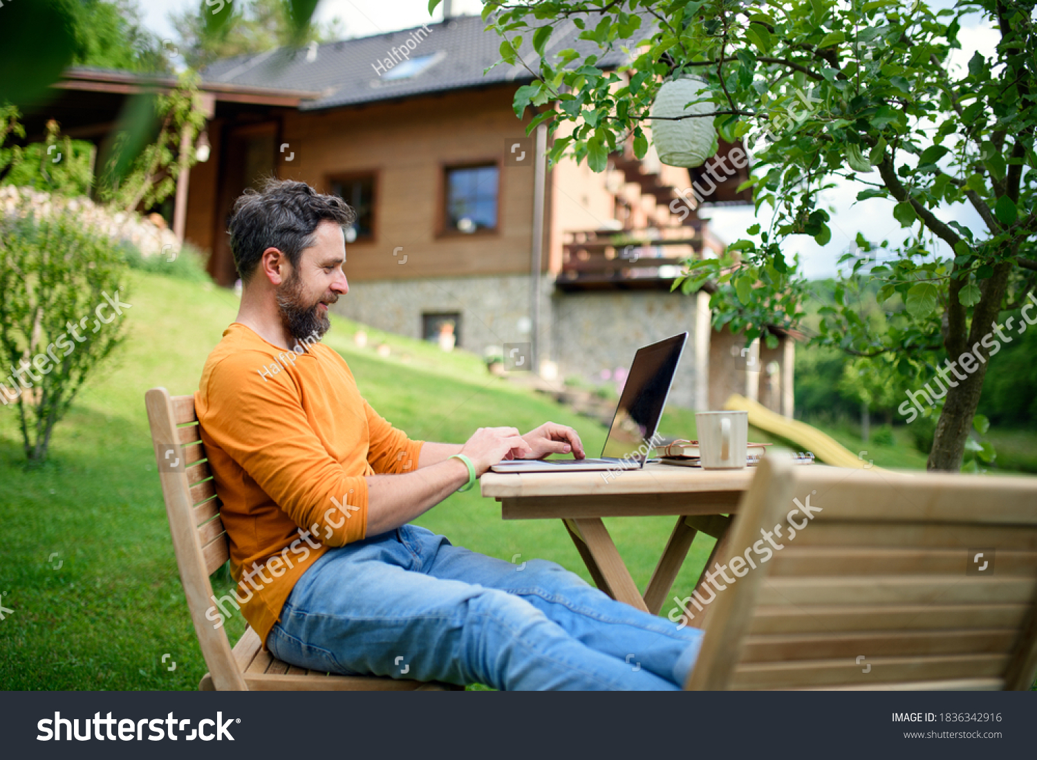Side view of man with laptop working outdoors in garden, home office concept. #1836342916