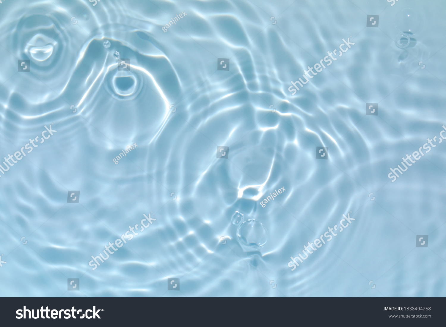 De-focused blurred transparent blue colored clear calm water surface texture with splashes and bubbles. Trendy abstract nature background. Water waves in sunlight with copy space. #1838494258
