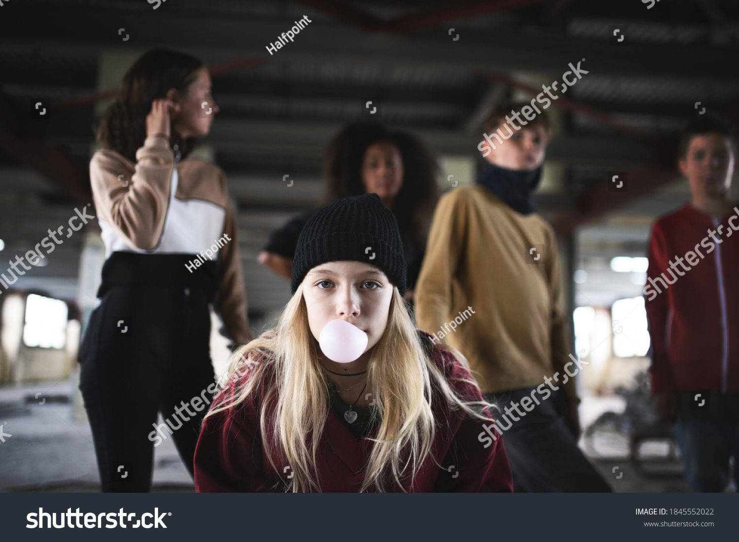 Teenager girl with friends standing indoors in abandoned building, making bubble gum. #1845552022
