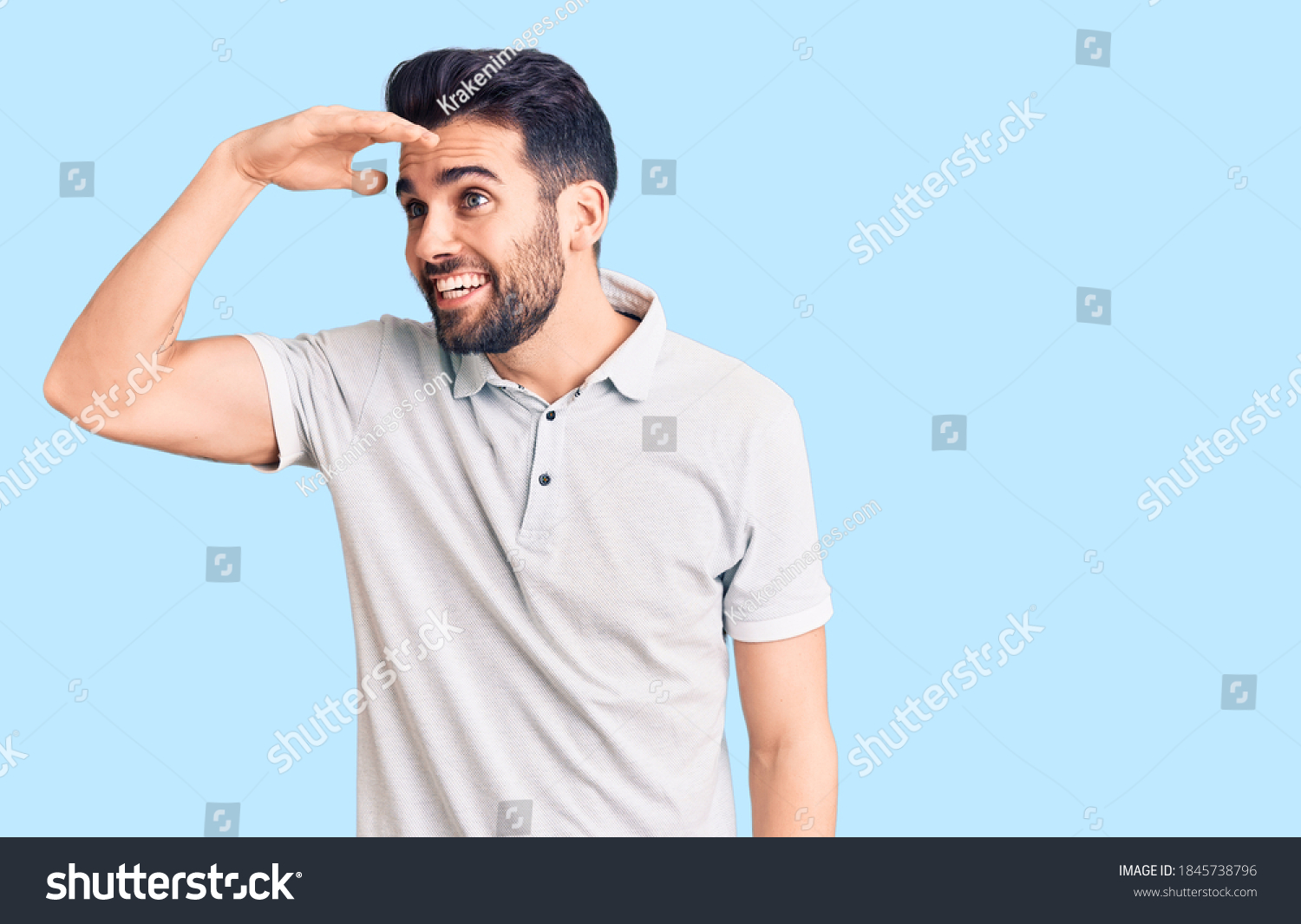 Young handsome man with beard wearing casual polo very happy and smiling looking far away with hand over head. searching concept.  #1845738796
