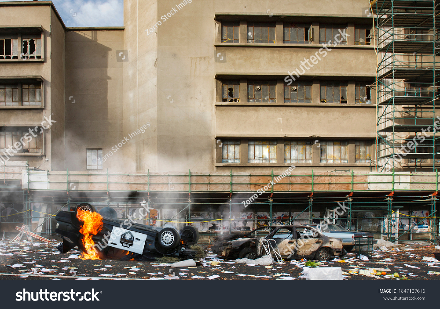 American riots and protests cause vandalism, looting and destruction, riot aftermath concept, upturned police car smashed on fire, broken windows of abandoned building, total anarchy and lawlessness #1847127616