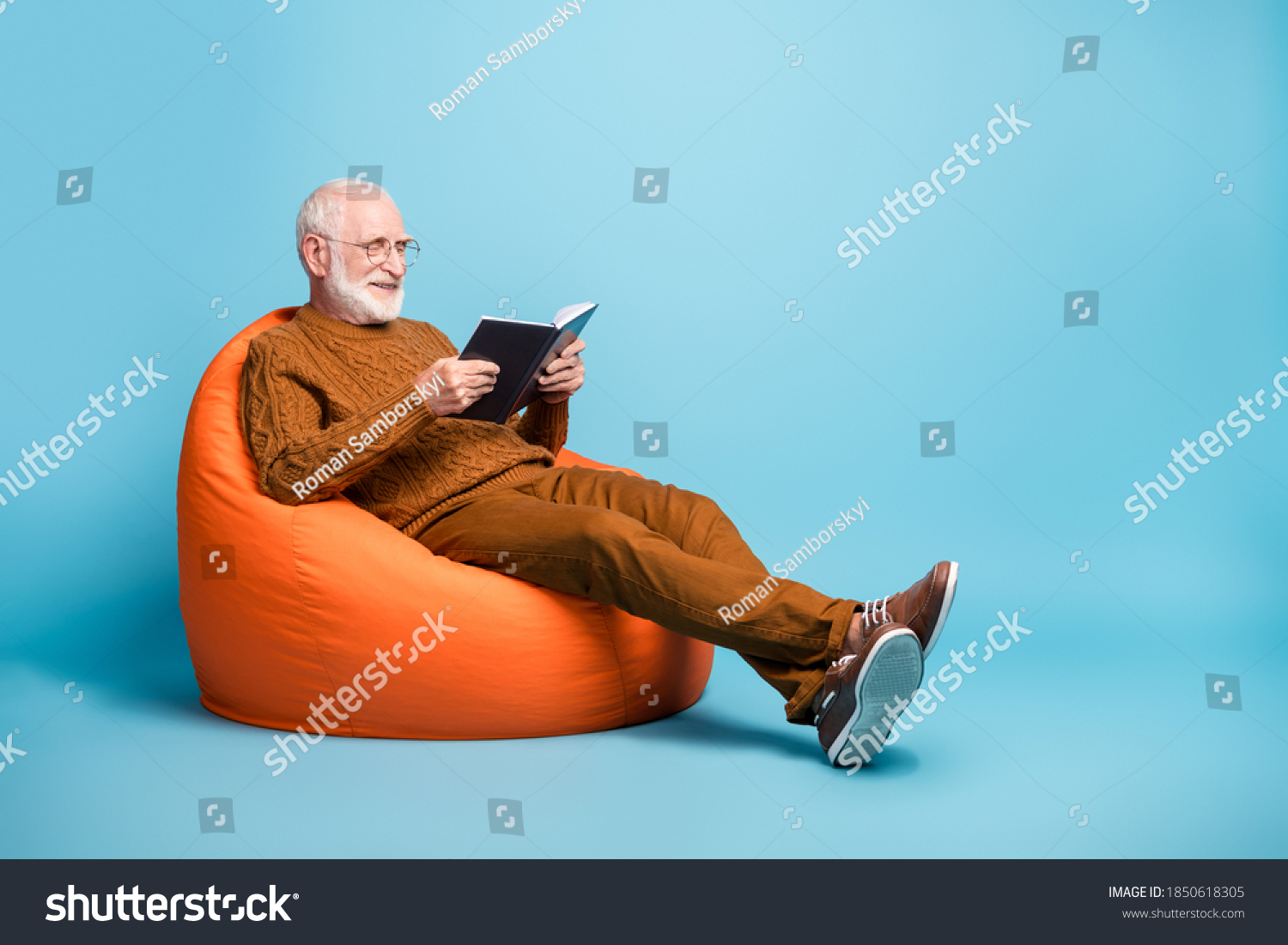 Portrait of his he nice attractive focused cheerful cheery wise smart clever bearded grey-haired man sitting in bag chair reading academic book isolated over blue pastel color background #1850618305