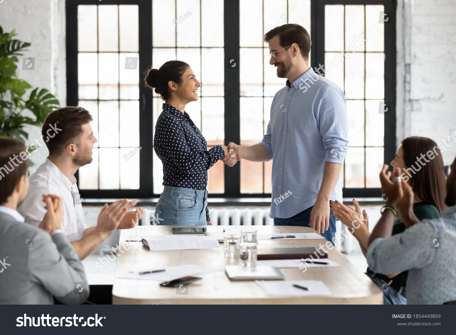 Young caucasian male ceo handshaking with indian female team member on briefing showing respect to her qualification, gratitude for help, recognition of her efforts in developing corporate business #1854449899