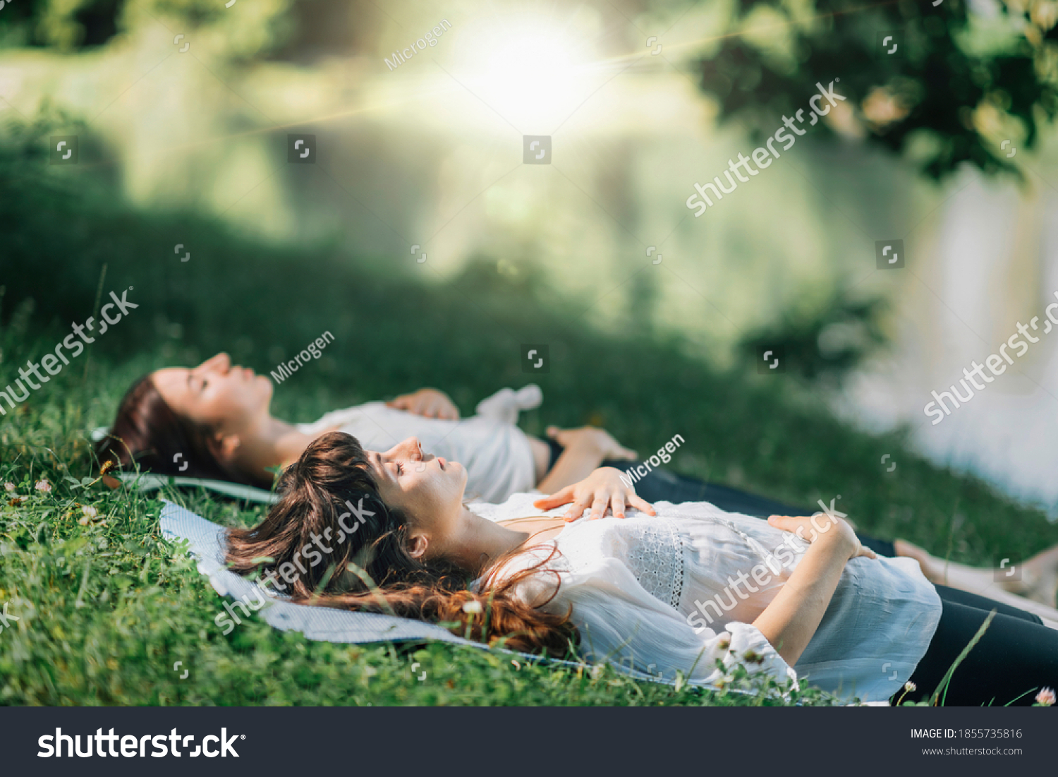 Meditation by the water. Two young women lying by the water and meditating #1855735816