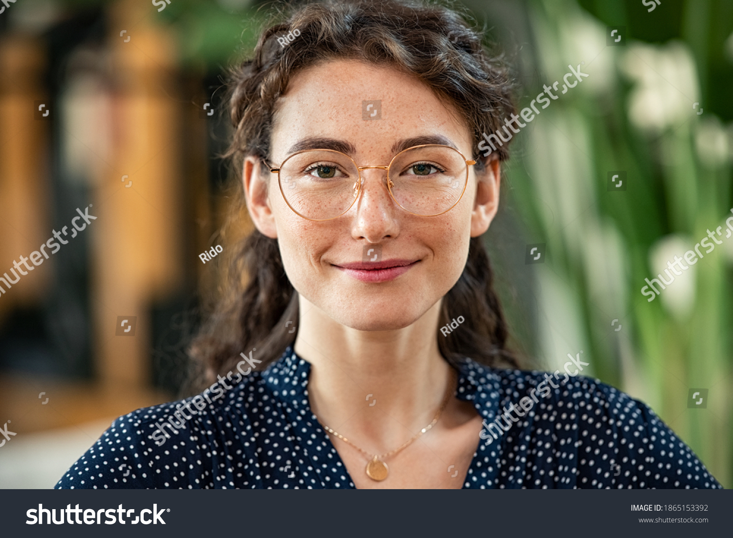Portrait of young woman wearing spectacles and looking at camera. Close up face of happy girl with glasses smiling at work. Confident and satisfied businesswoman wearing eyeglasses in office. #1865153392