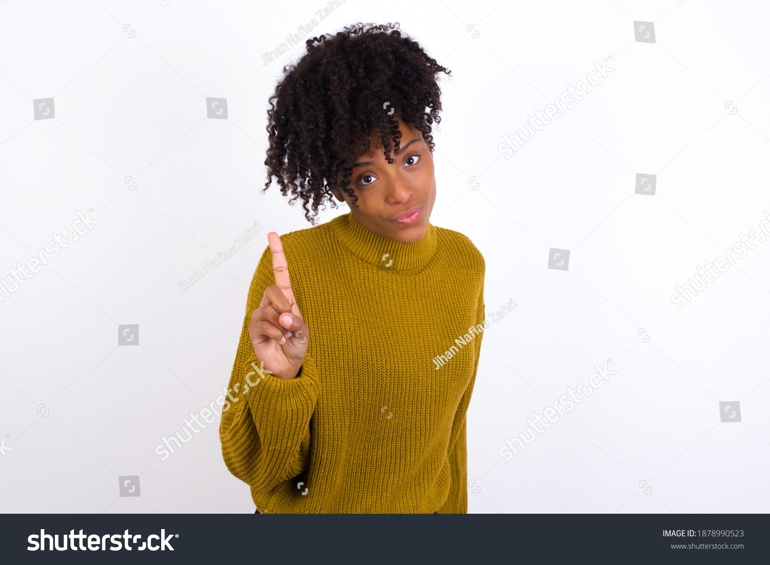 No sign gesture. Closeup portrait unhappy Young beautiful African American woman wearing knitted sweater against white wall raising fore finger up saying no. Negative emotions facial expressions, feel #1878990523
