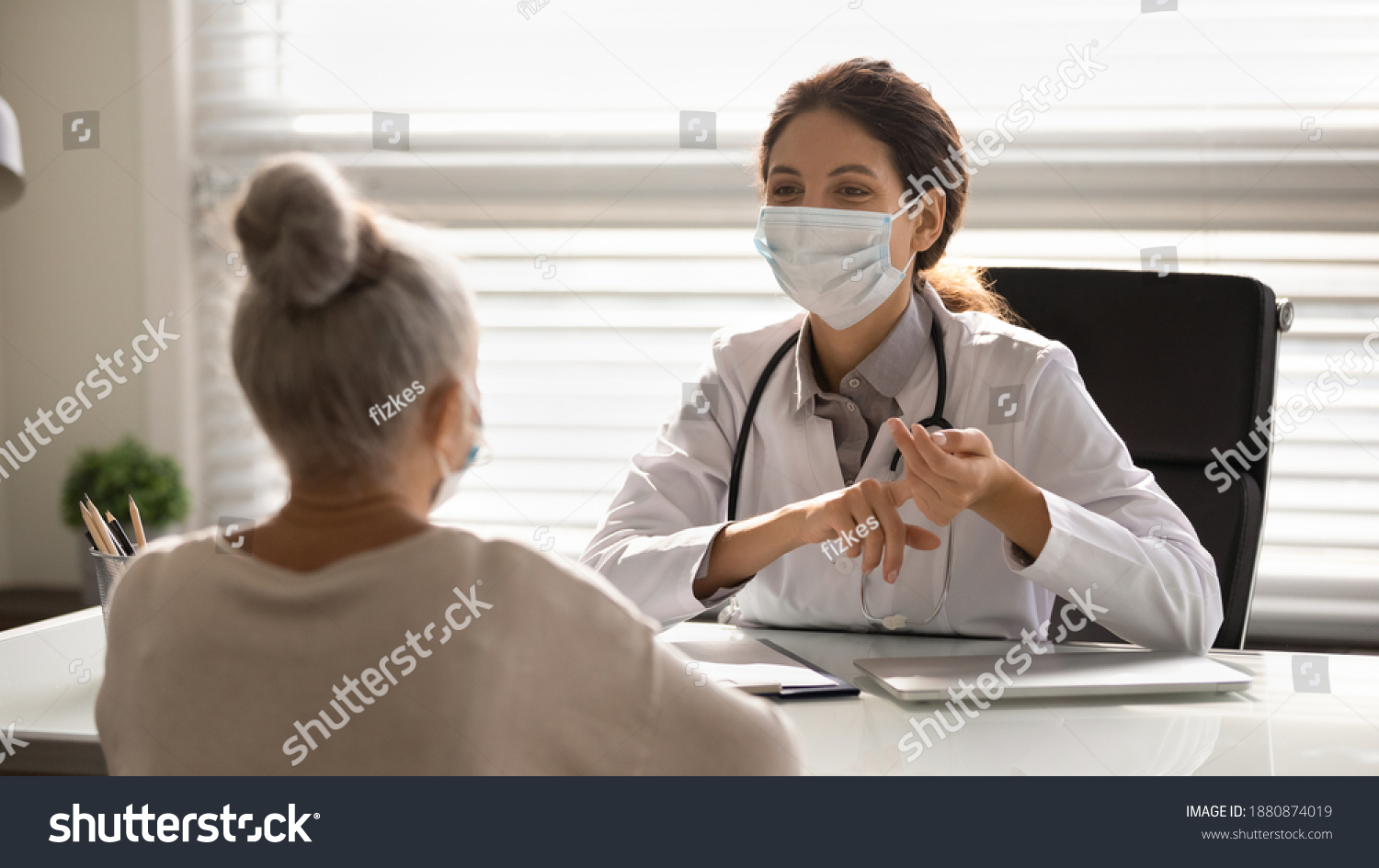 Female doctor in medical facial mask have consultation with elderly patient during covid-19 pandemics. Woman GP in facemask talk consult mature client in clinic or hospital. Coronavirus concept. #1880874019