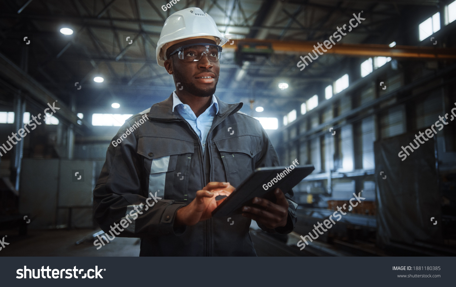 Professional Heavy Industry Engineer Worker Wearing Safety Uniform and Hard Hat Uses Tablet Computer. Smiling African American Industrial Specialist Walking in a Metal Construction Manufacture. #1881180385