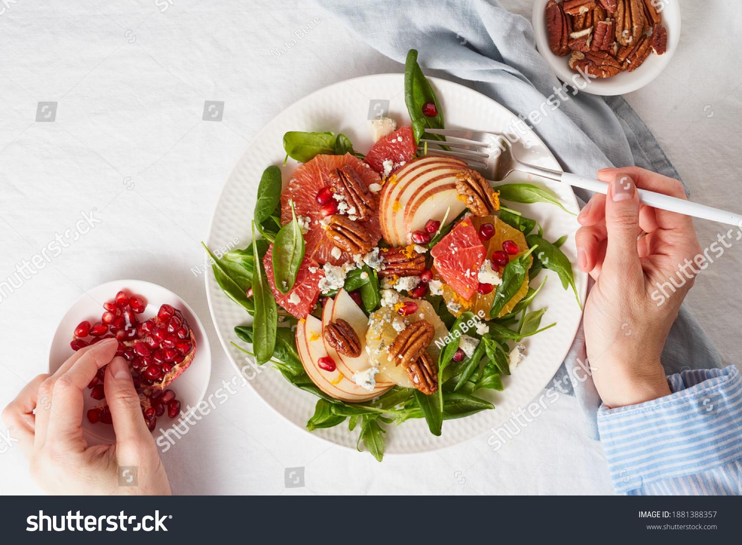 Eating fruits citrus salad with nuts, green lettuce. Balanced food. Top view of woman hands with plate of meal of Spinach with orange, grapefruit, apples, pecans #1881388357