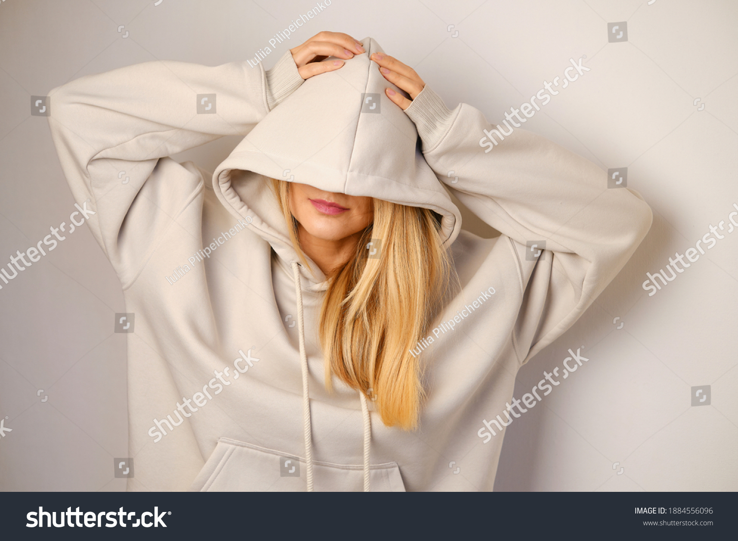 Young beautiful girl in a white hoodie posing. Warm oversized hoodie with an hood. Stylish trendy hipster bow. Trying on clothes in a store. Youth subculture. Fashion clothing advertising #1884556096
