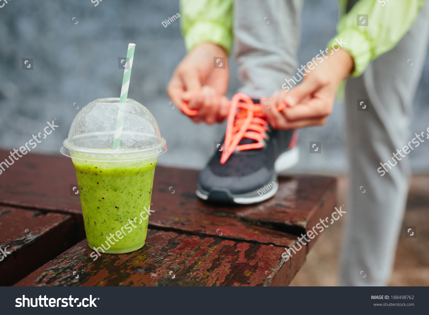 Green detox smoothie cup and woman lacing running shoes before workout on rainy day. Fitness and healthy lifestyle concept. #188498762