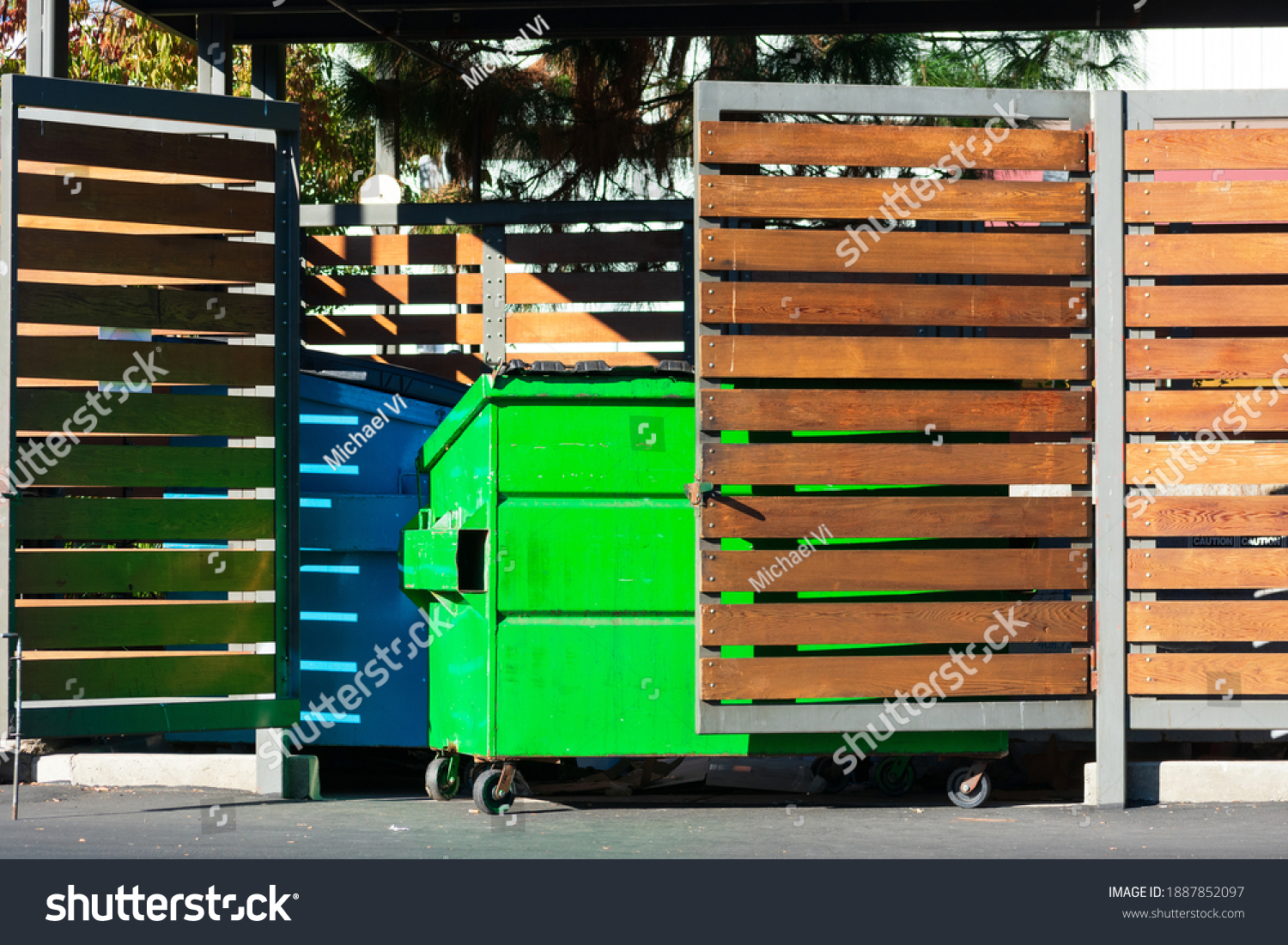 Two waste management blue and green garbage containers dumpsters in garbage enclosure used for commercial and residential garbage. #1887852097