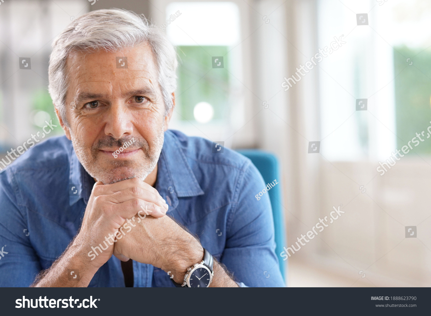Portrait of 60-year-old man with grey hair and blue shirt looking at camera #1888623790