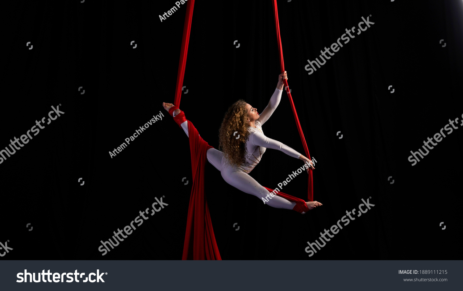 Professional aerialist circus performer on red bright aerial silks performs balance on a splits #1889111215