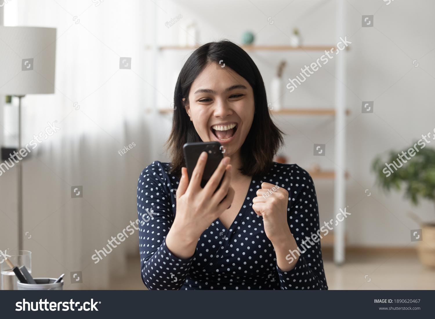 Emotional happy millennial korean ethnicity woman looking at smartphone screen, reading message with unbelievable amazing news, celebrating getting online shopping prize or lottery win notification. #1890620467