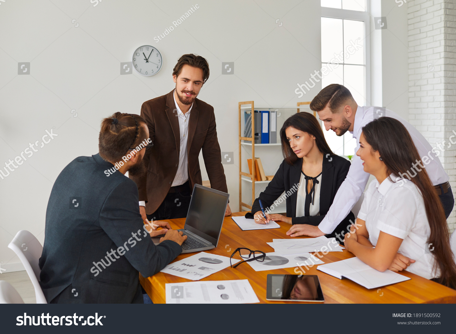 Startup group meeting around office desk in creative workspace. Start-up leader listening to teammates' suggestions, talking, discussing budget issues and work needs. Sales team analyzing results #1891500592