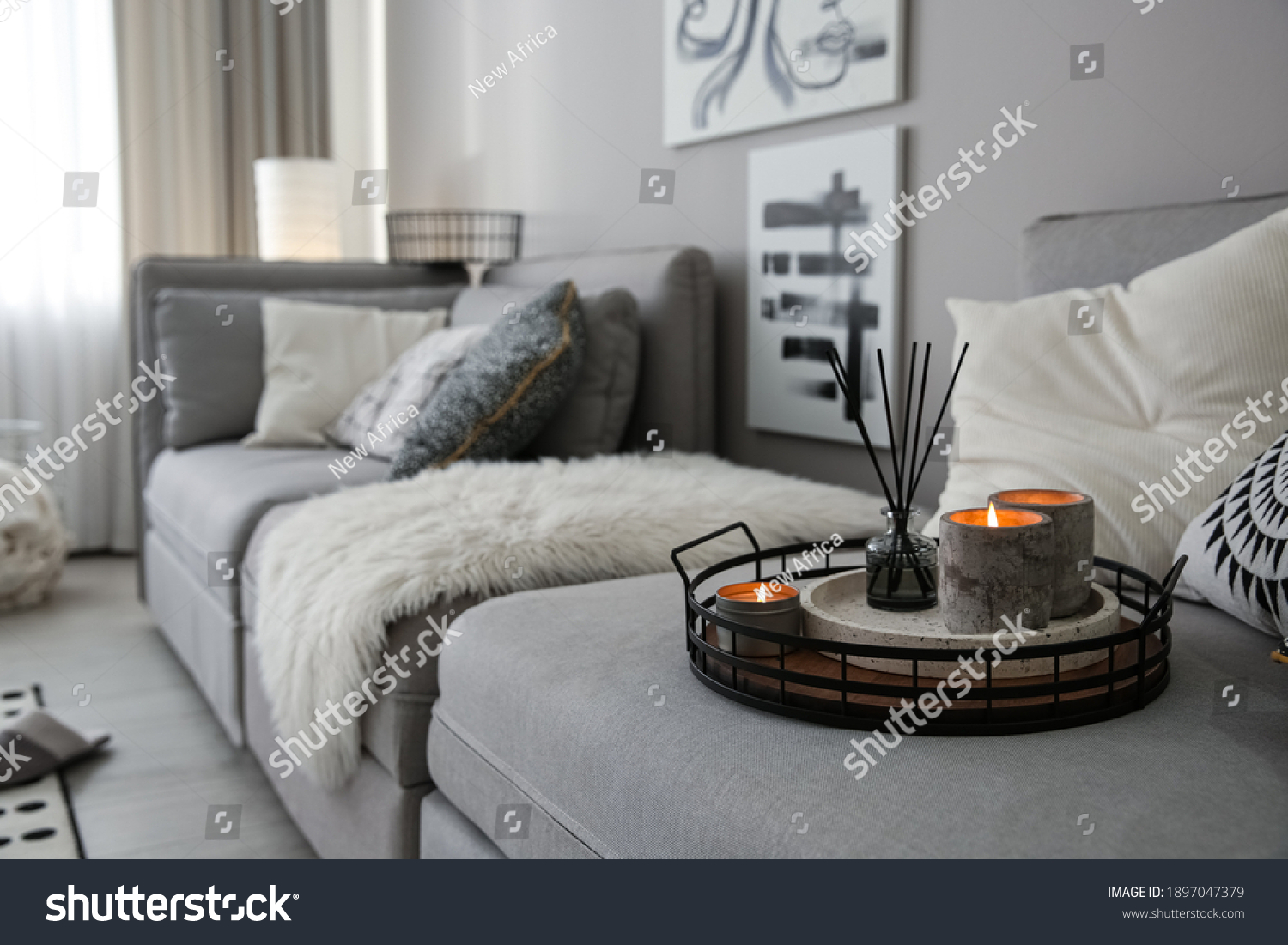 Candles and aroma reed diffuser on grey sofa, space for text #1897047379