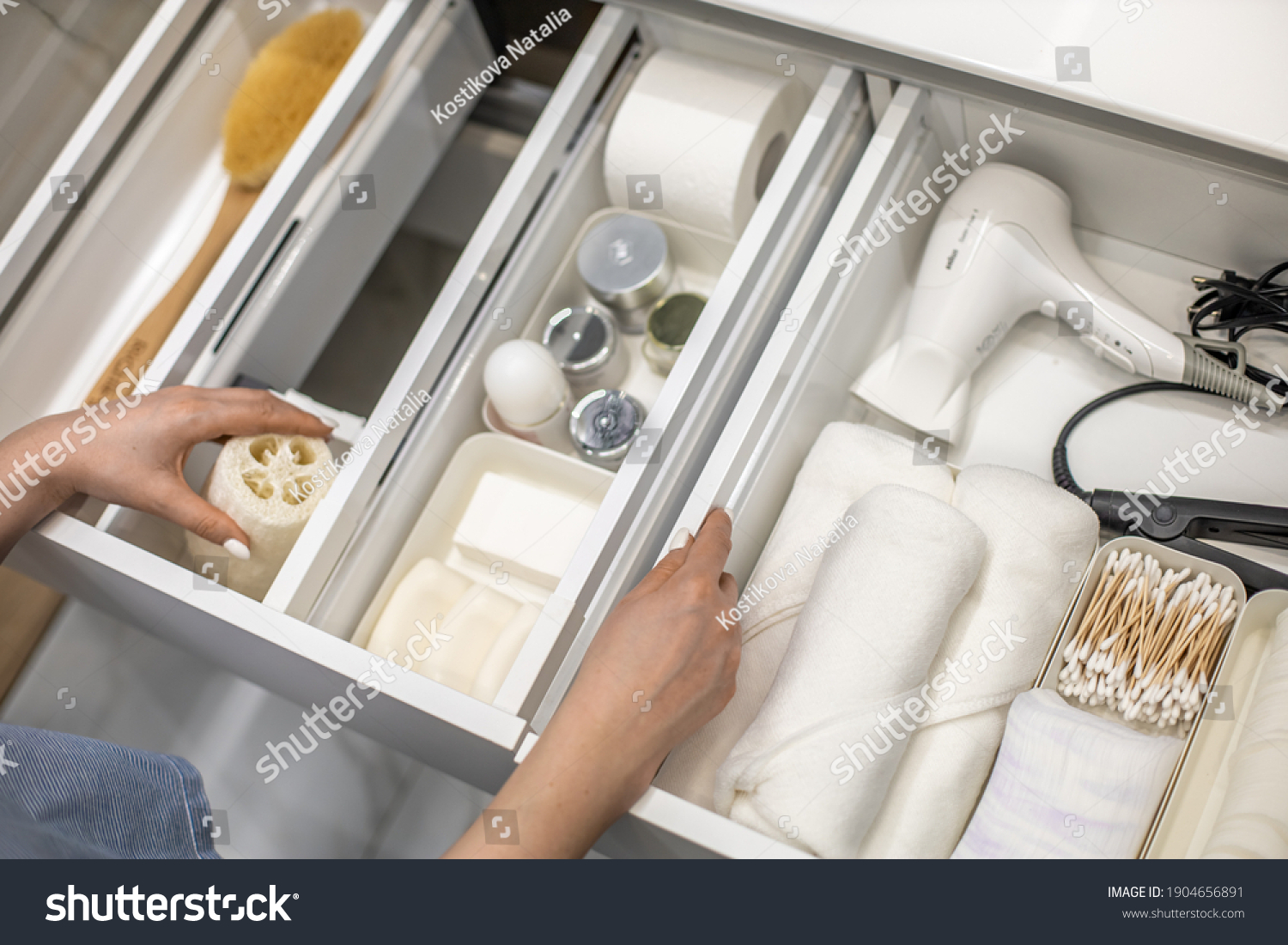 Top view of woman hands neatly organizing bathroom amenities and toiletries in drawer or cupboard in bathroom. Concept of tidying up a bathroom storage by using Marie Kondo's method. #1904656891