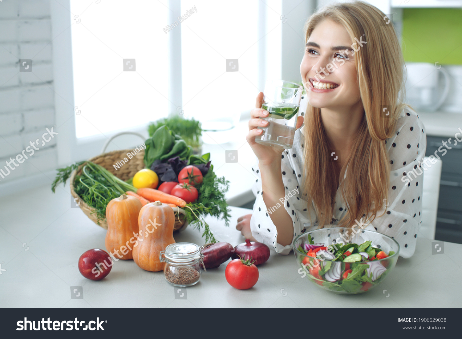 Woman on a diet. Young and happy woman eating healthy salad sitting on the table with green fresh ingredients indoors. High quality photo #1906529038