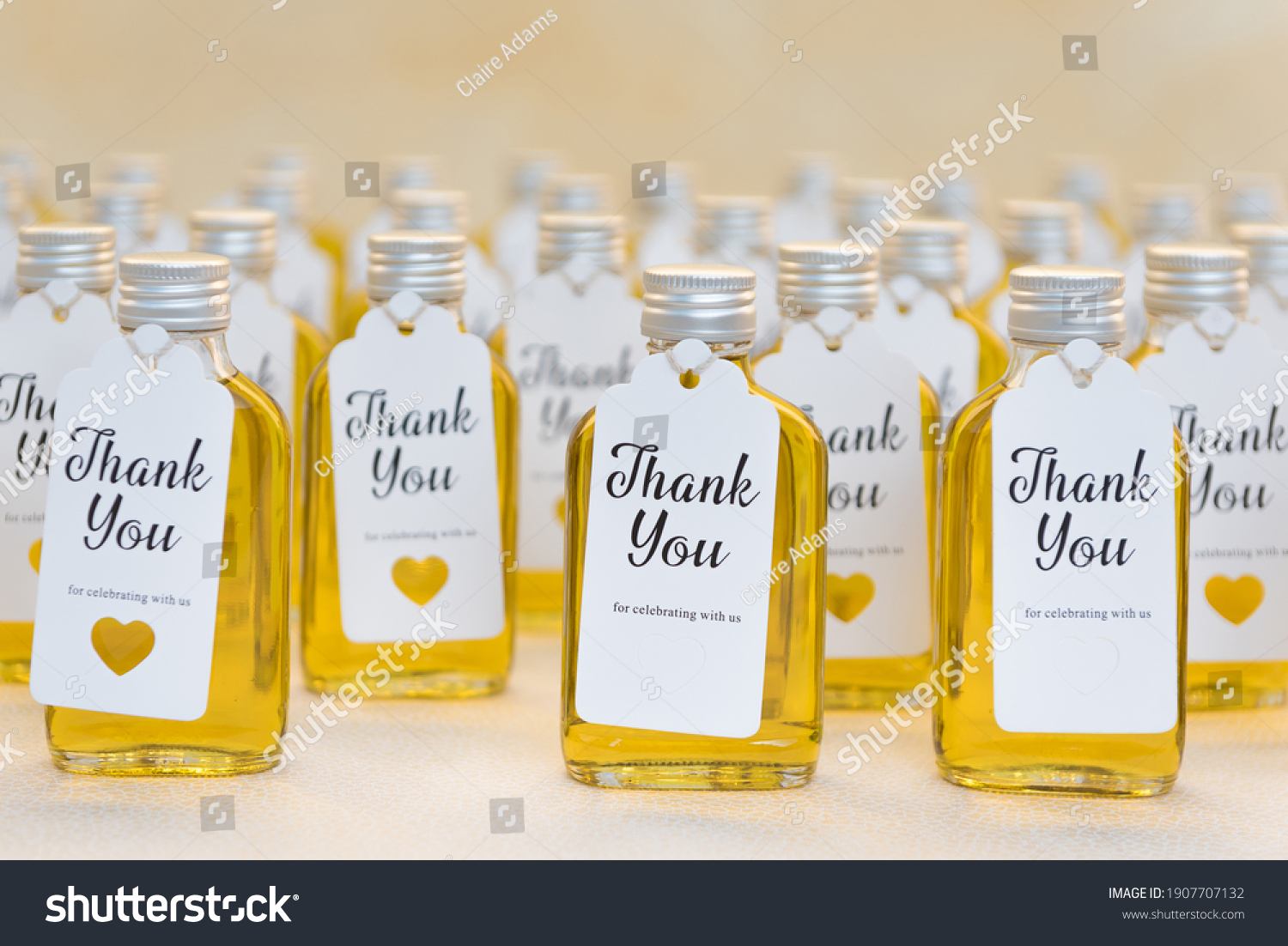 Rows of small twist-cap bottles filled with yellow liquid (oil, honey, bubble bath, massage oil) with thank-you cards attached to the front, with space for message or text #1907707132
