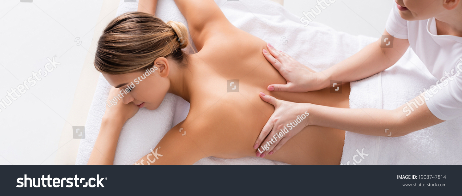 high angle view of happy masseur massaging back of young client on massage table, banner #1908747814