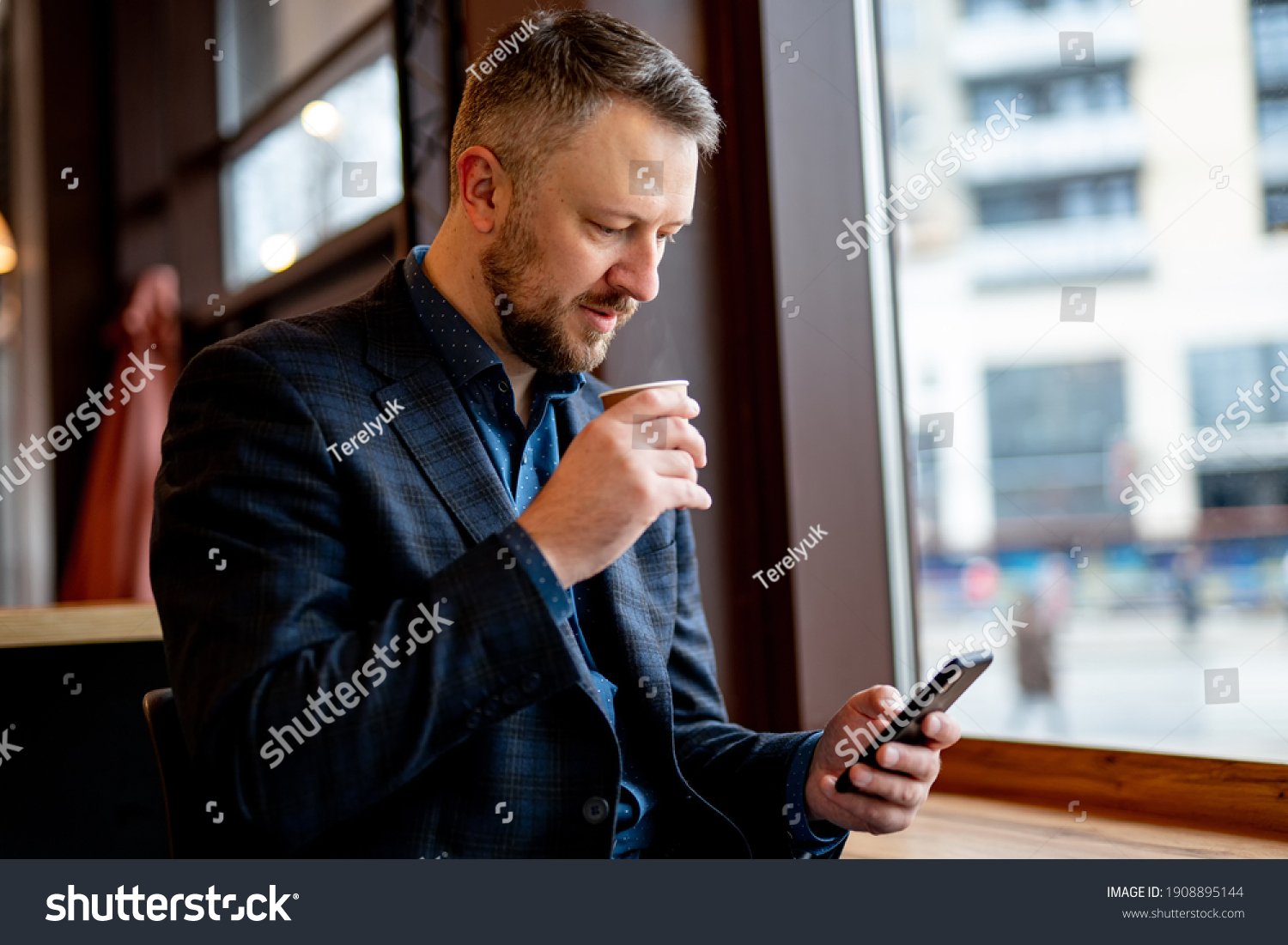 Authentic image of a pensive businessman in a coffee shop. Businessman in dark suit having break surfing internet on the phone. #1908895144
