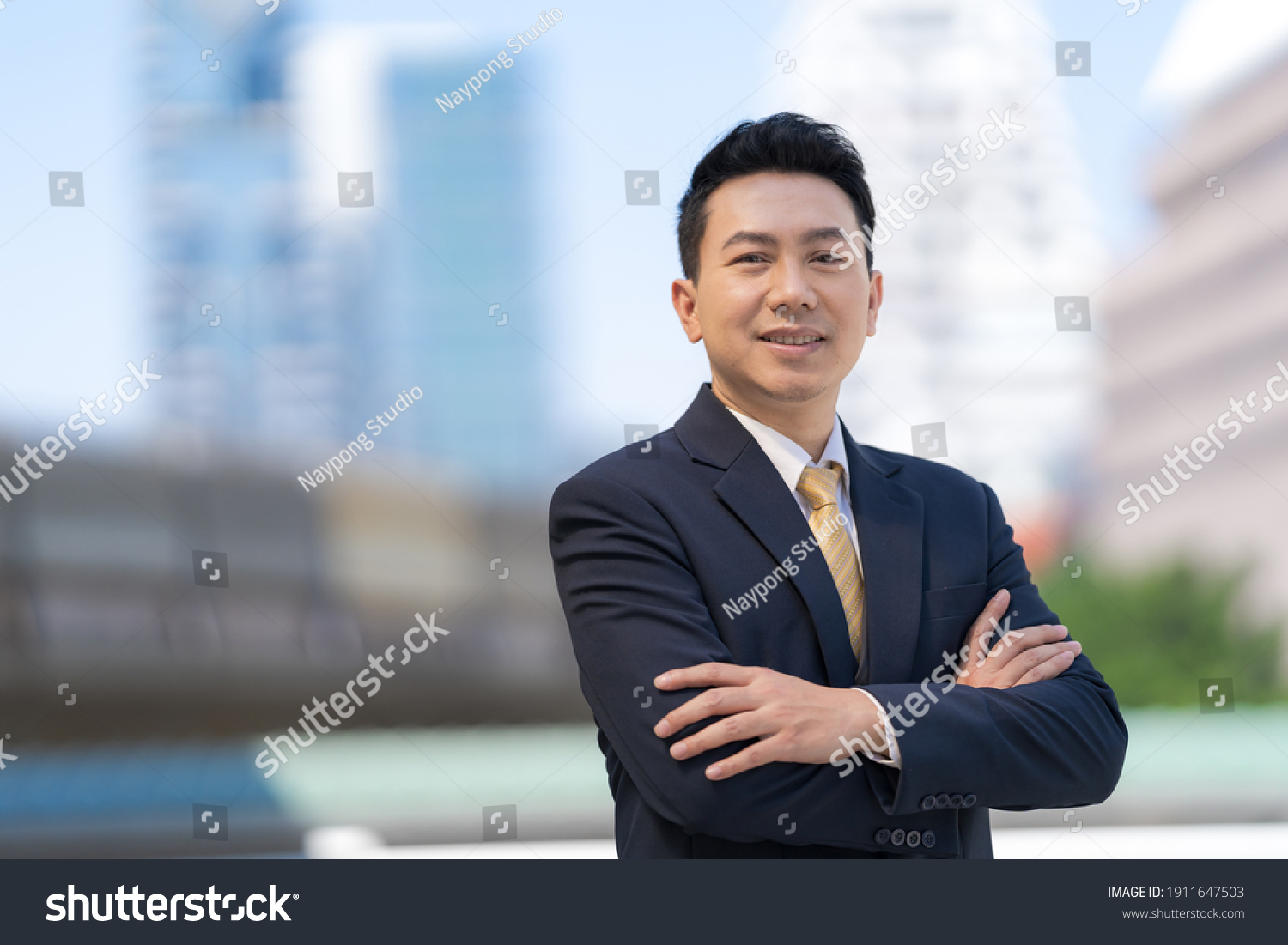 Portrait of successful asian businessman standing with arms crossed standing in front of modern office buildings #1911647503