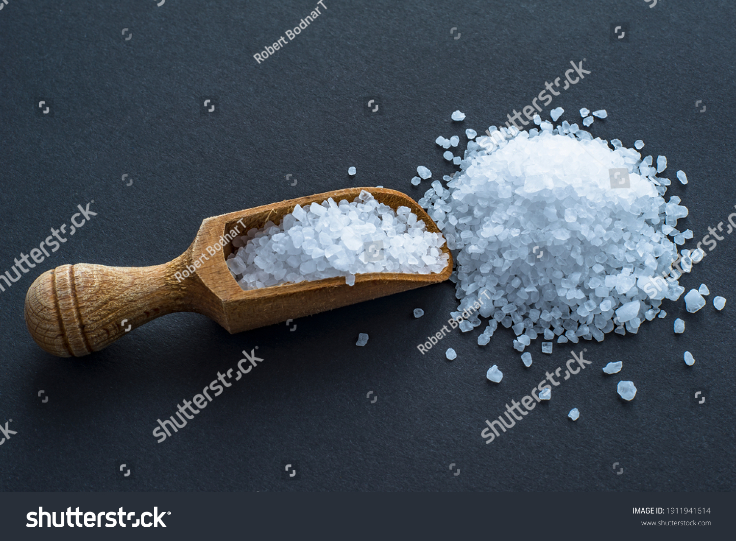 wooden spoon with coarse salt on a black background.  #1911941614