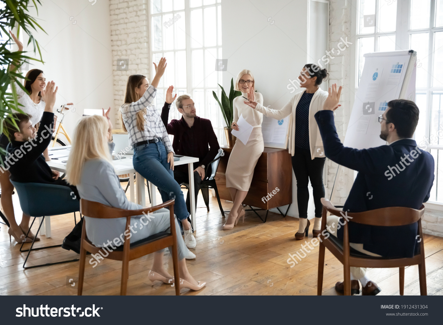 Motivated employees raising hands, asking coach at training. Presenter finishing workshop with questions from engaged audience. Indian female business leader interacting with team at corporate meeting #1912431304