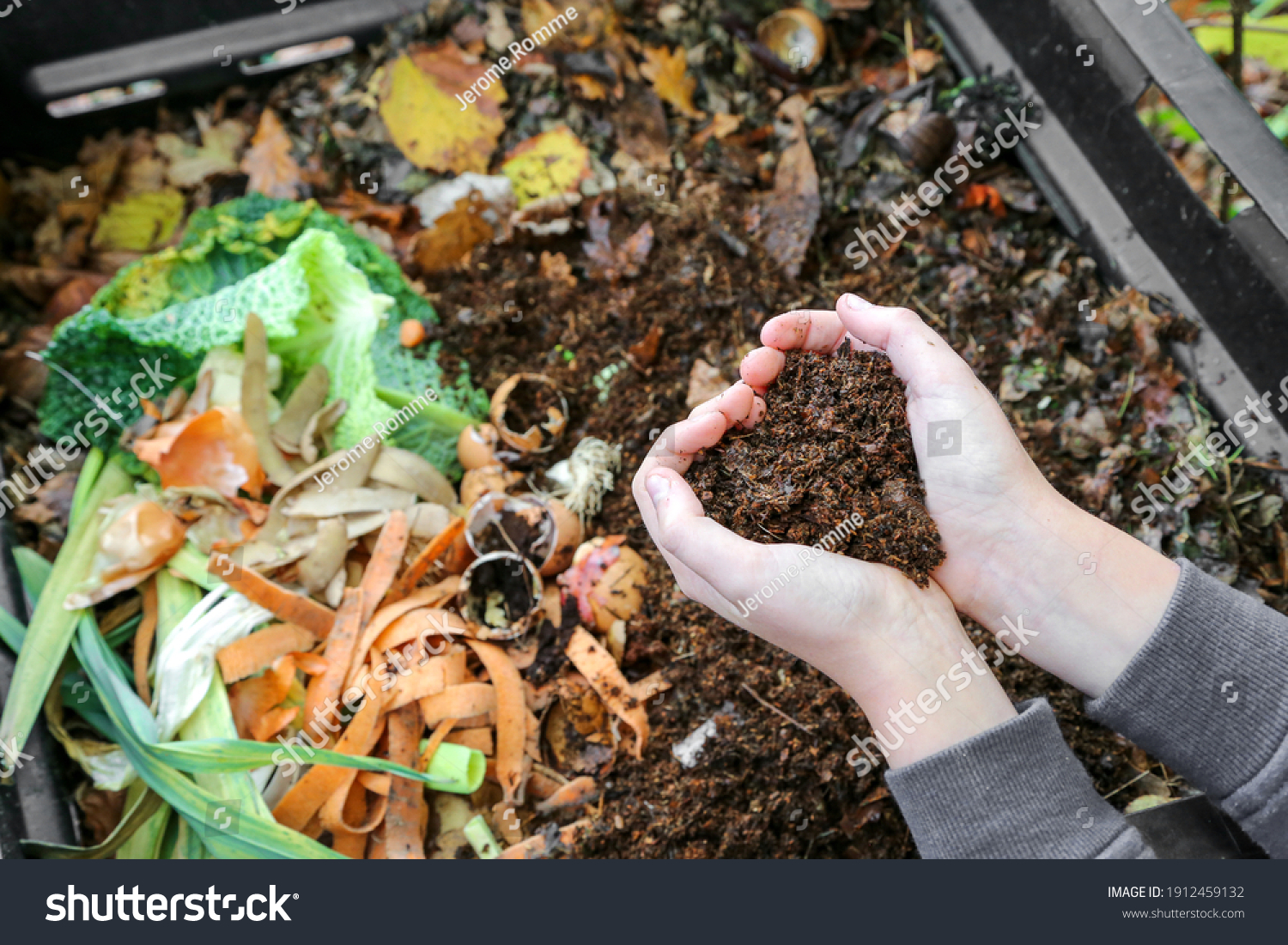 hands holding compost above the composter with organic waste #1912459132