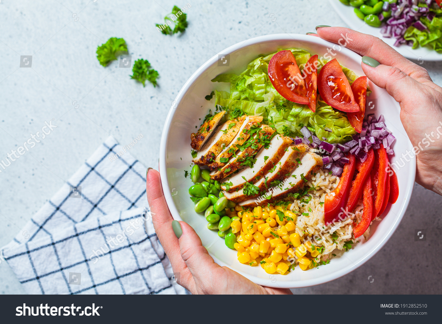 Grilled chicken breast with brown rice and vegetables in a white plate, gray background. Healthy food concept. #1912852510