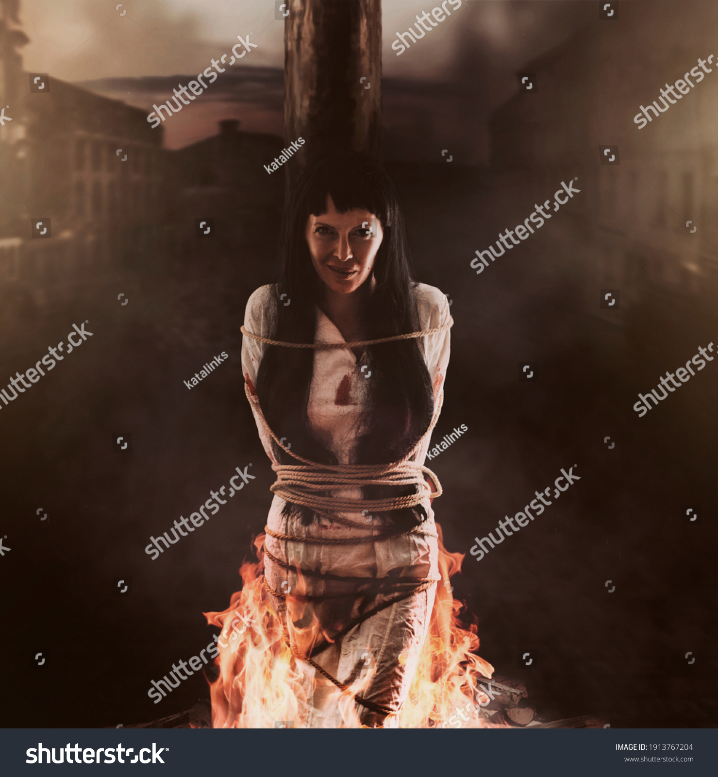 Medieval witch is tied to a wooden post and burns at the stake and smile #1913767204